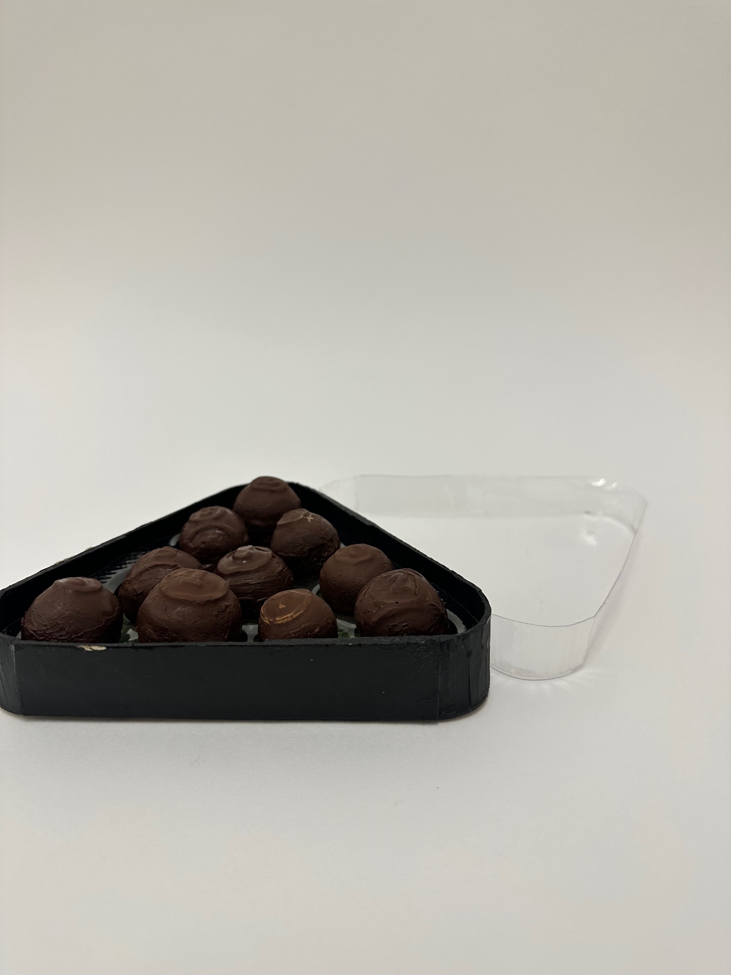 Triangle rack of cast chocolate pool balls beside a clear plastic shell.
