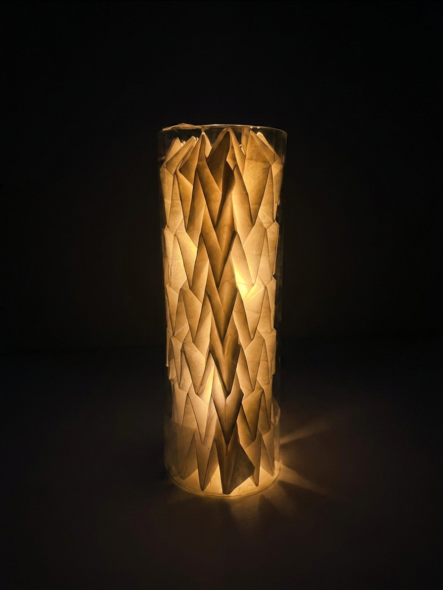 The same paper lantern photographed in darkness, glow emphasizing the folded pattern.
