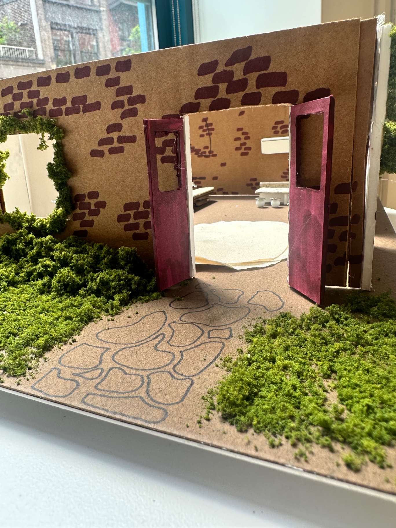 Detail of the model's entry: red doors framed in a hand-stamped brick wall with moss garden and stepping stones.